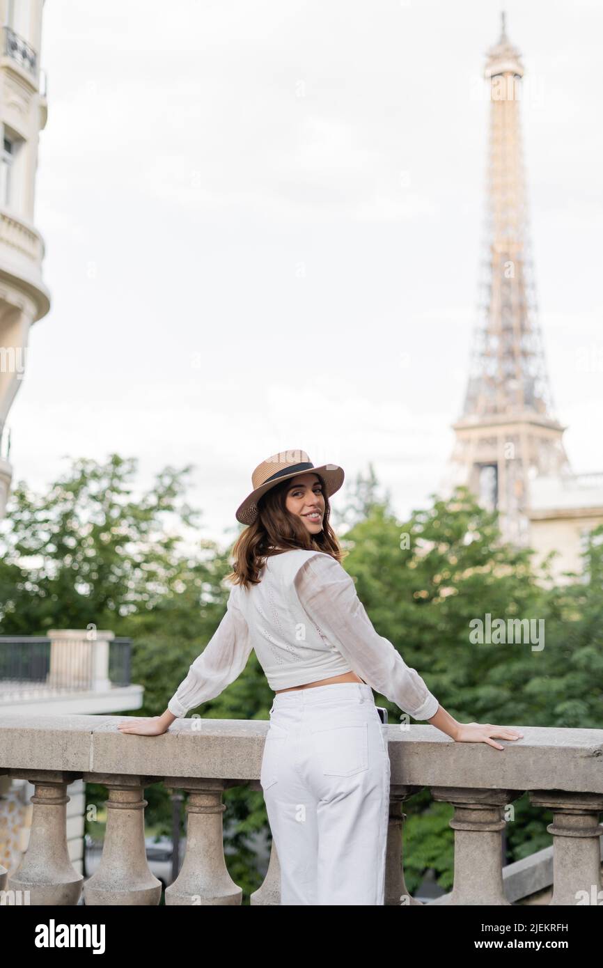 Il viaggiatore allegro in cappello di paglia che guarda la macchina fotografica con la torre Eiffel sullo sfondo in Francia Foto Stock