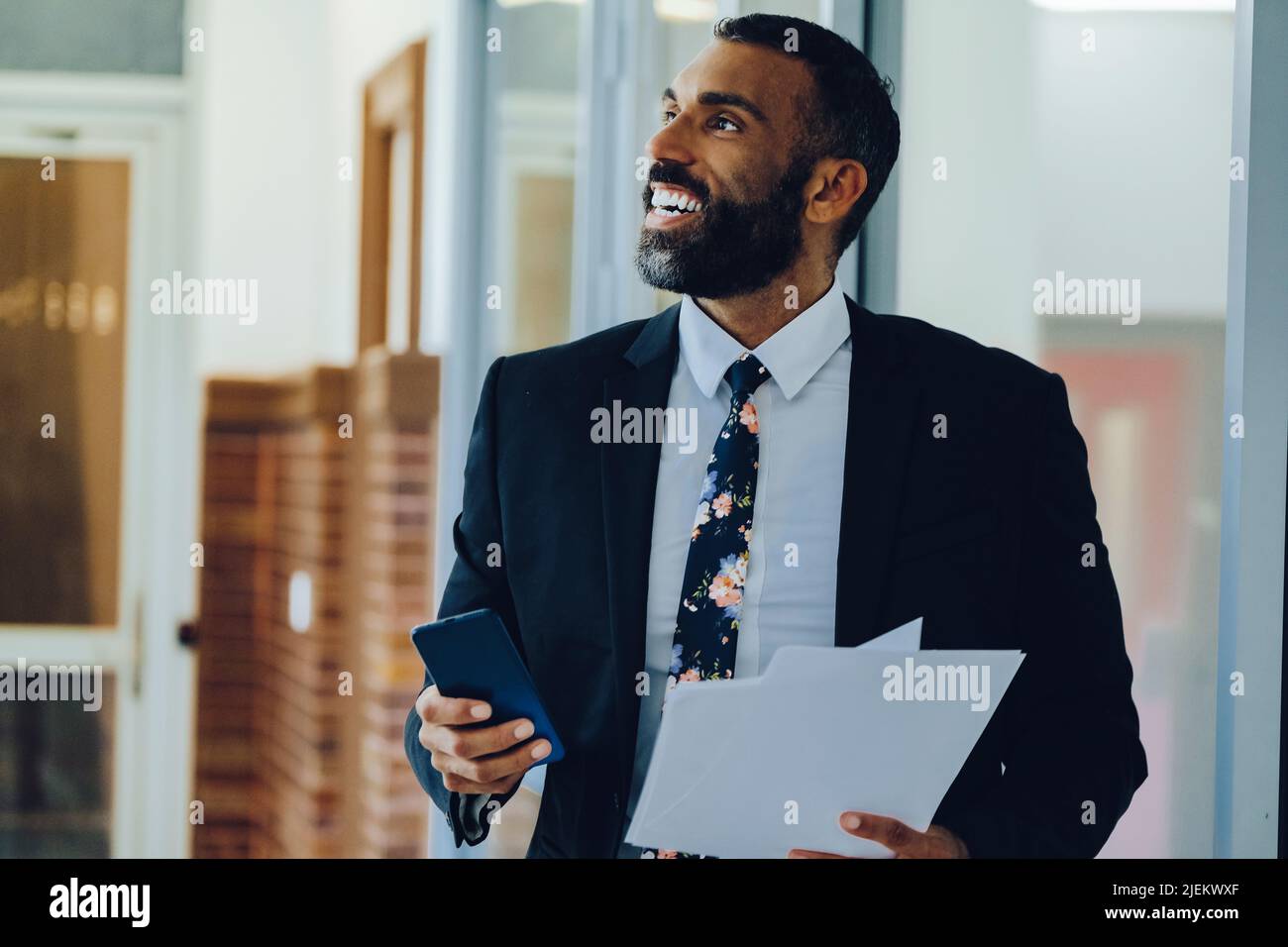 Uomo d'affari dell'imprenditore uomo d'affari medio adulto bearded uomo d'affari che indossa il vestito che tiene le carte e la camminata dello smartphone in ufficio colpo Foto Stock