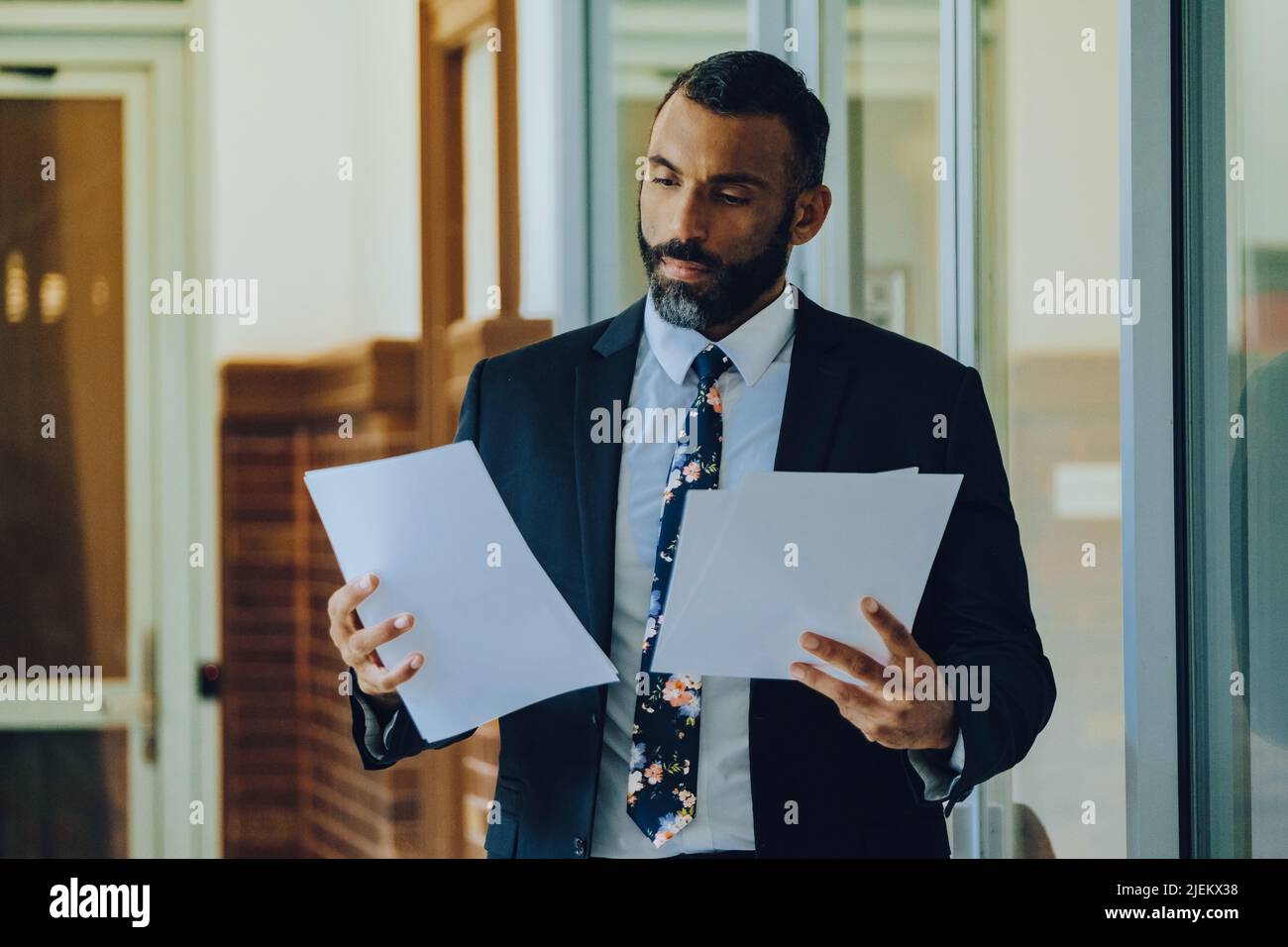 MID adulto bearded uomo nero imprenditore uomo d'affari che indossa il vestito che tiene le carte che camminano nel colpo d'ufficio Foto Stock