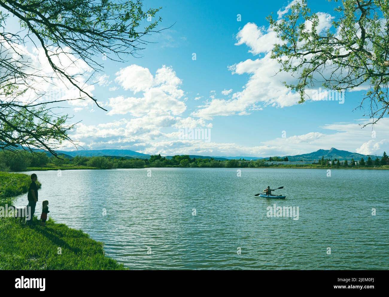 Kayak sul lago Beck a Cody, Wyoming, con Heart Mountain sullo sfondo. Gli osservatori sono sulla riva. I riflessi della nuvola sono nell'acqua. Foto Stock