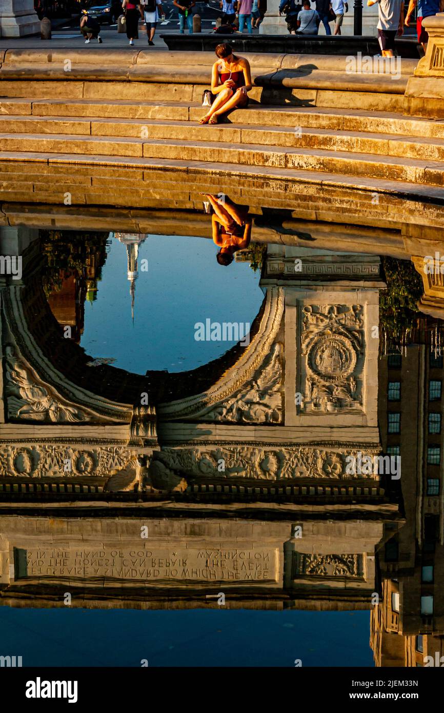 Una donna e un arco monumentale si riflettono nella fontana del Washington Square Park a New York City Foto Stock