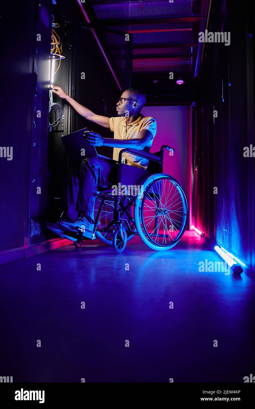 Ritratto completo della persona con disabilità che lavora presso l'amministratore di sistema nella sala server illuminata da luce al neon Foto Stock