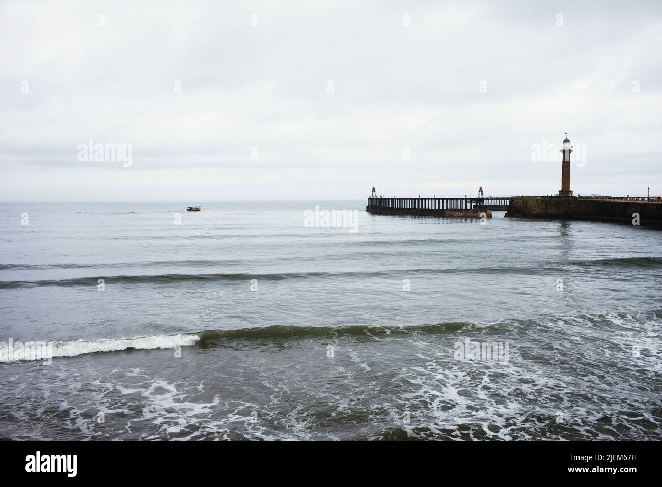 Il molo esterno ovest al porto di Whitby con una piccola barca in lontananza. Foto Stock