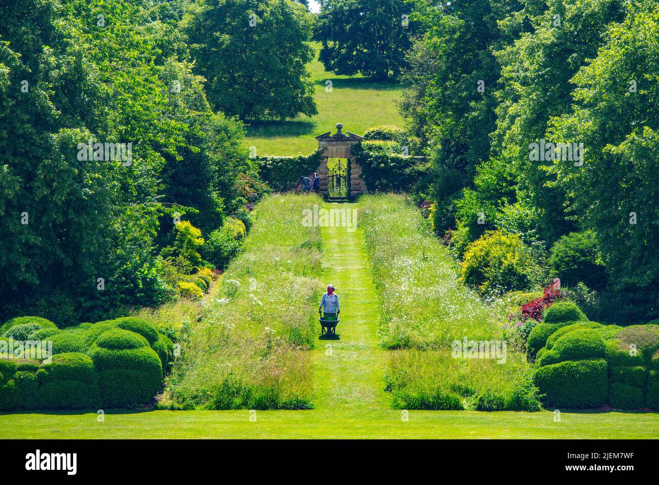 Una vista da Nunnington Hall - un giardiniere volontario ruota una carriola nel bellissimo terreno di una casa signorile del National Trust Foto Stock