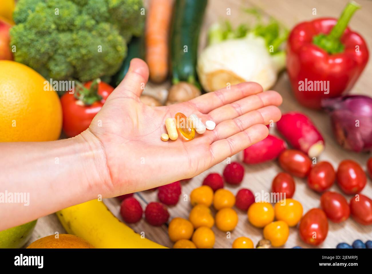 Mano sta tenendo le tovlette di supplemento di cibo sopra una tabella di legno piena di verdure e frutta. Gli integratori alimentari consentono uno stile di vita sano. Foto Stock