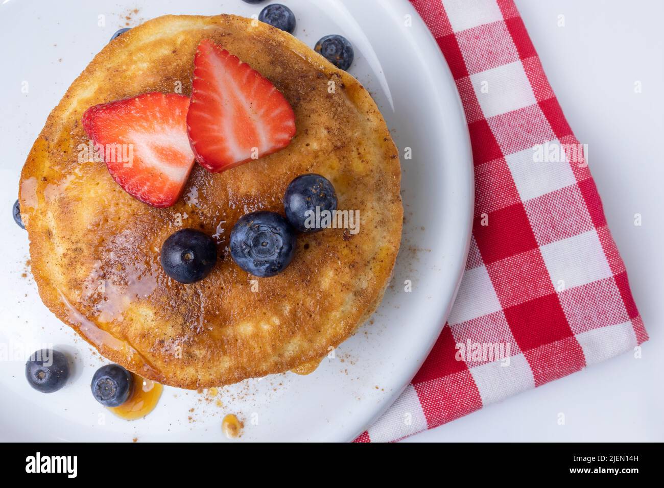 Pancake americani con sciroppo d'acero, fragole e mirtilli per colazione su un piatto vista dall'alto con una tradizionale tovaglia da picnic Foto Stock