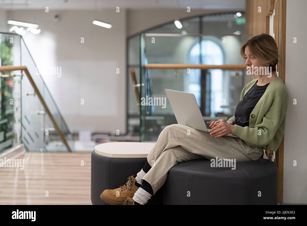 Donna incentrante e pensiva freelance che lavora su un notebook in biblioteca Foto Stock