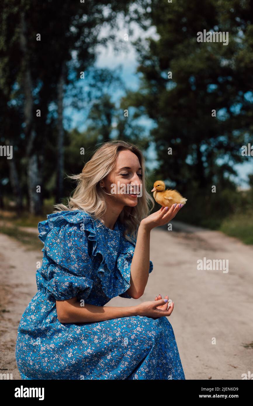 Una ragazza in un abito lungo blu accoccolato e tiene un anatroccolo nelle  sue mani Foto stock - Alamy
