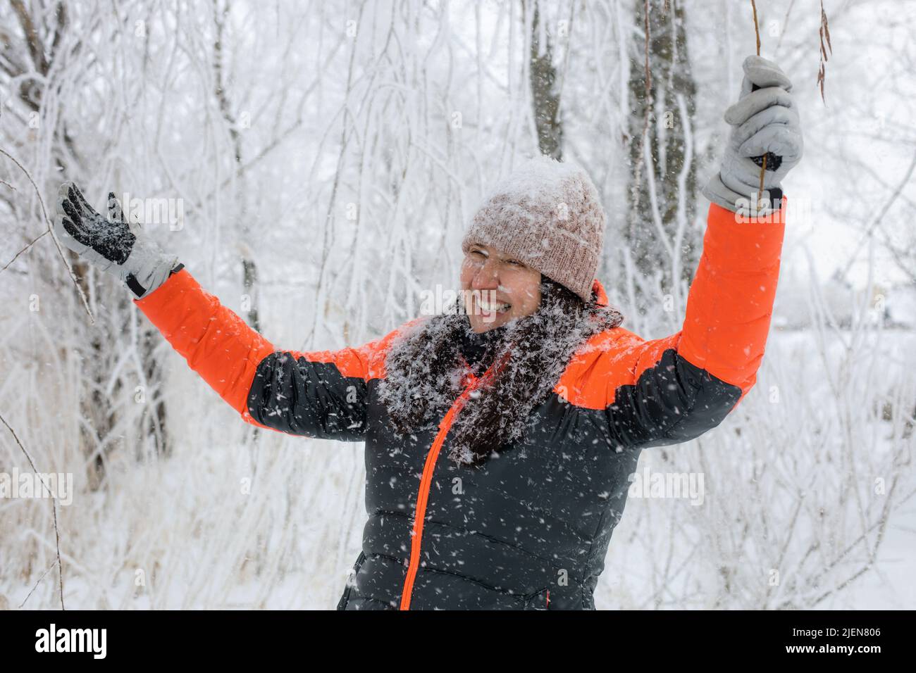 Ridendo donna di mezza età con le braccia distese guardando via camminare in foresta nevosa con la neve che cade su di lei. Magico tempo invernale pieno di bianco Foto Stock