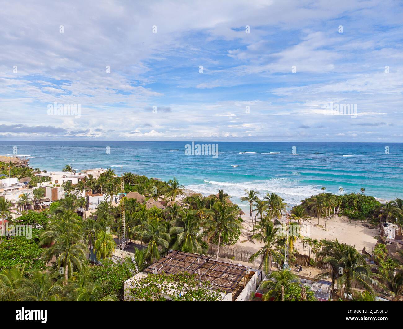 Vista oceano della spiaggia di Tulum con palme verdi e proprietà sulla spiaggia in una giornata nuvolosa con il blu del Mar dei Caraibi Foto Stock