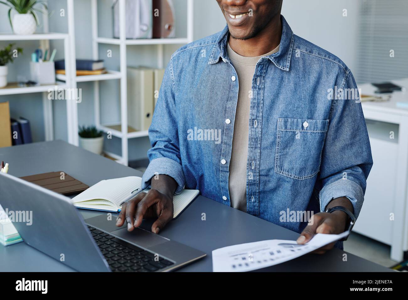 Ritratto ritagliato di giovane data scienziato utilizzando un computer portatile in ufficio e sorridente Foto Stock