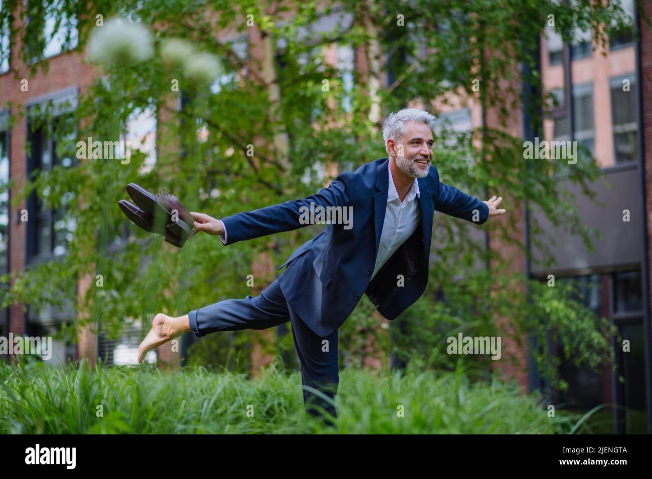 Ritratto divertente di uomo d'affari maturo e energico felice che porta scarpe e camminare a piedi nudi e fare posa in parco, sentirsi liberi, lavoro equilibrio della vita Foto Stock