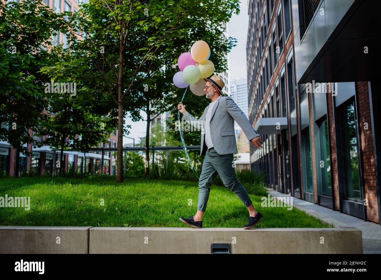 Ritratto divertente di uomo d'affari maturo felice energico tenendo palloncini e camminare sul muro, sentirsi liberi, lavoro vita equilibrio concetto. Foto Stock
