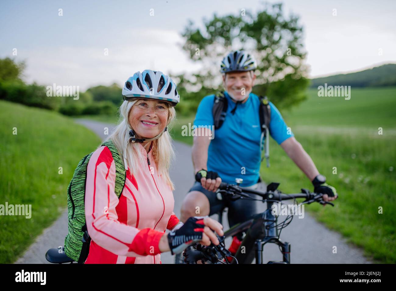 Active Senior Couple a cavallo di biciclette elettriche su strada al parco estivo, concetto di stile di vita sano. Foto Stock