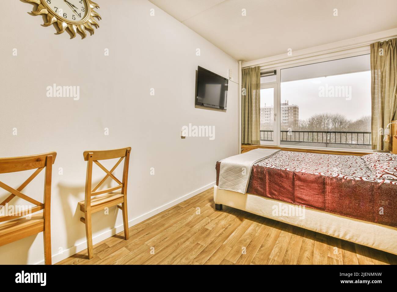 Comodo letto situato vicino alla porta del balcone con tende in una camera da letto accogliente e luminosa a casa Foto Stock