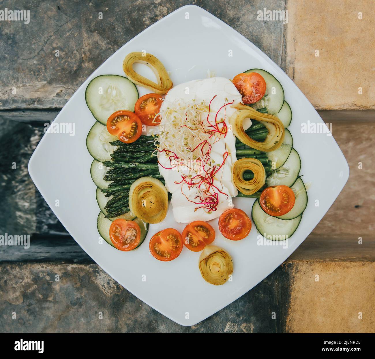 Piatto bianco con cibo biologico vegetale originariamente decorato con molti colori e tavolo sullo sfondo Foto Stock