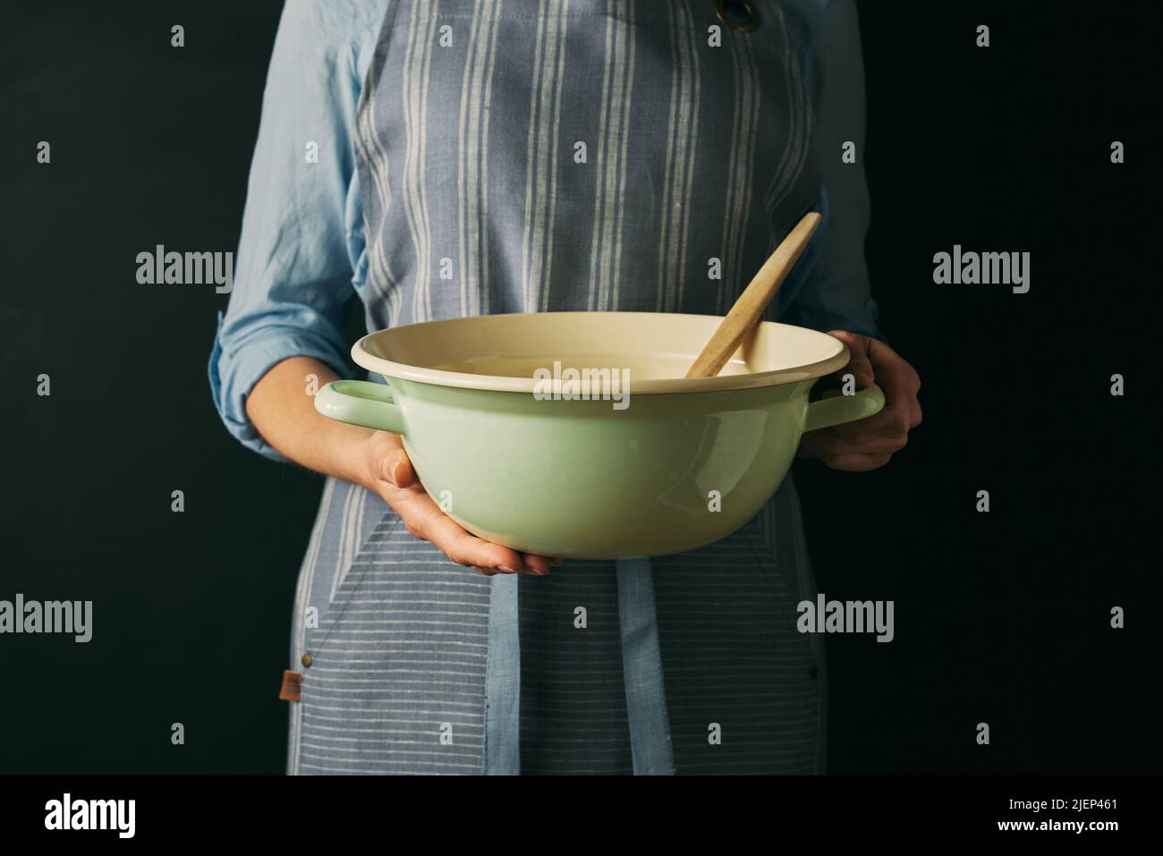 Crop anonimo cuoco femminile in grembiule tenere ciotola con spatola mentre si prepara per la cottura su sfondo nero in studio moderno Foto Stock
