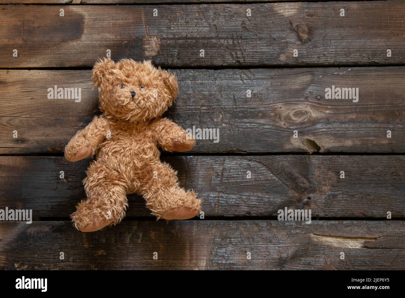 un vecchio orsacchiotto marrone giace solo su un pavimento di legno bruciato, un giocattolo per bambini sul pavimento Foto Stock