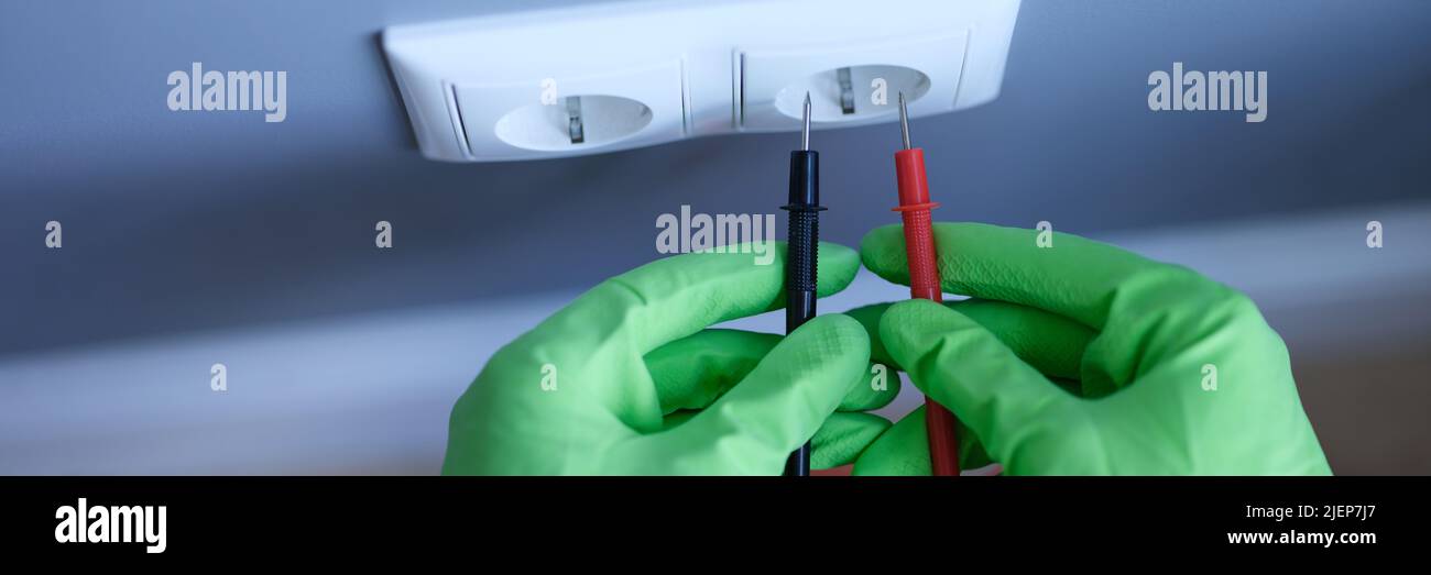 Le mani con i guanti tengono un multimetro digitale vicino alla presa Foto Stock