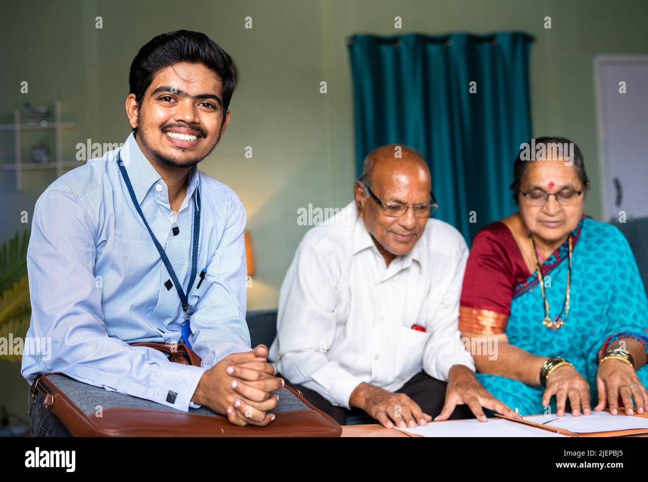 Felice sorridente banchiere guardando la macchina fotografica di fronte alla coppia anziana a casa - concetto di servizio di home banking, consulente finanziario e personale di supporto. Foto Stock