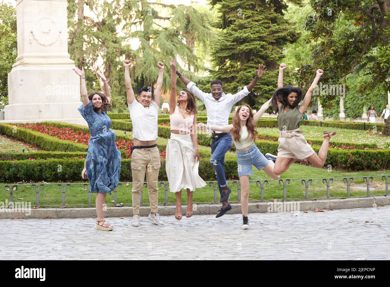 Gruppo di amici multietnici sorridenti e saltano mentre si diverte all'aperto in un parco. Concetto di amicizia. Foto Stock