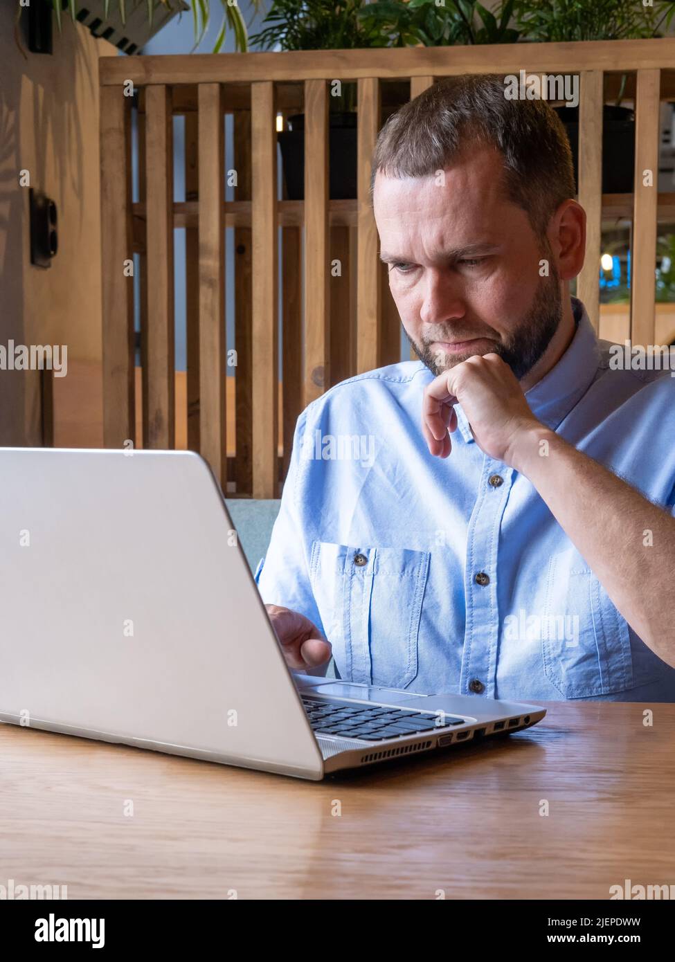 L'uomo arabo serio e bello con la barba sta usando il laptop, leggendo la posta elettronica, digitando sulla tastiera nel caffè. Bel freelance maschile che lavora sul laptop al lavoro Foto Stock