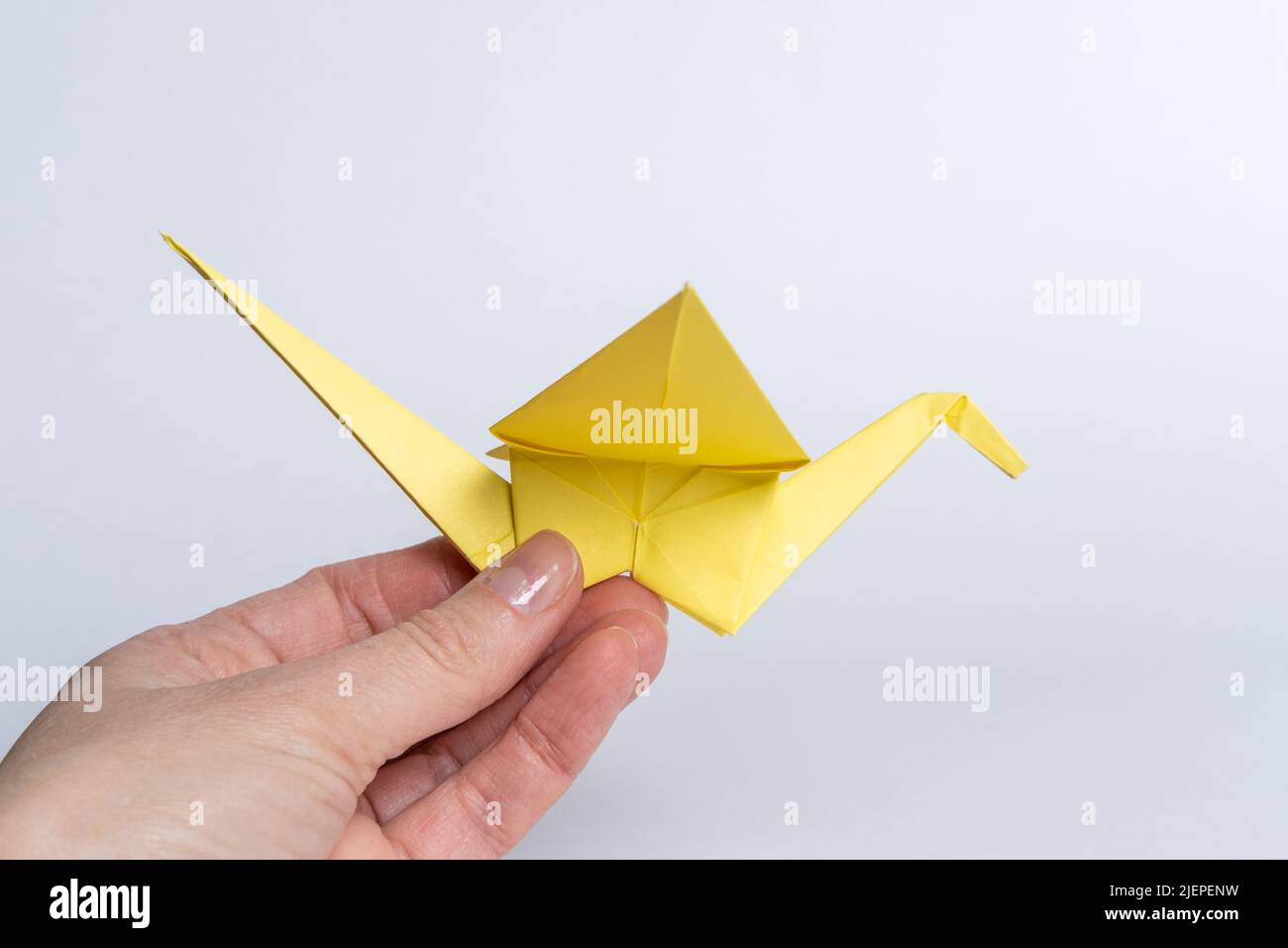 Gru tradizionali giapponesi in carta gialla su sfondo bianco. Una mano che tiene un uccello di carta. Creatività dei bambini. Un simbolo di pace. Foto Stock