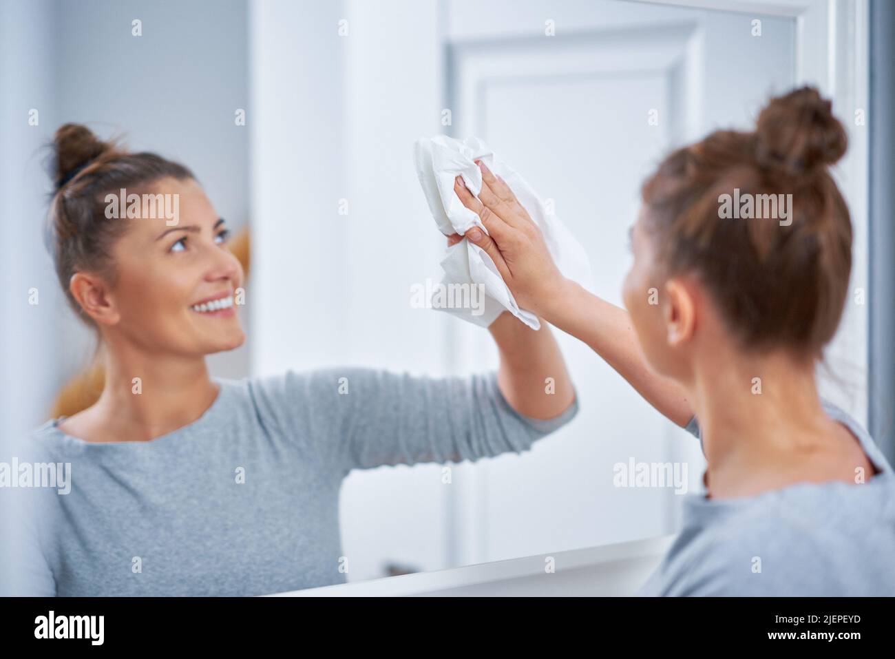 Immagine della donna più giovane che pulisce la finestra dello specchio Foto Stock