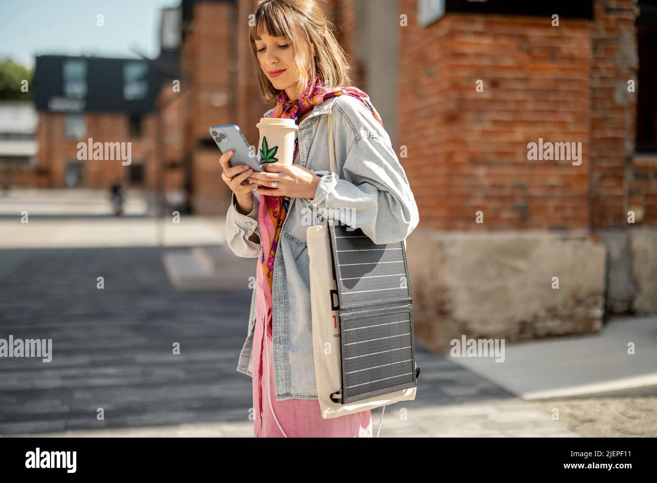 Donna carica il telefono dal pannello solare portatile mentre cammina all'aperto Foto Stock
