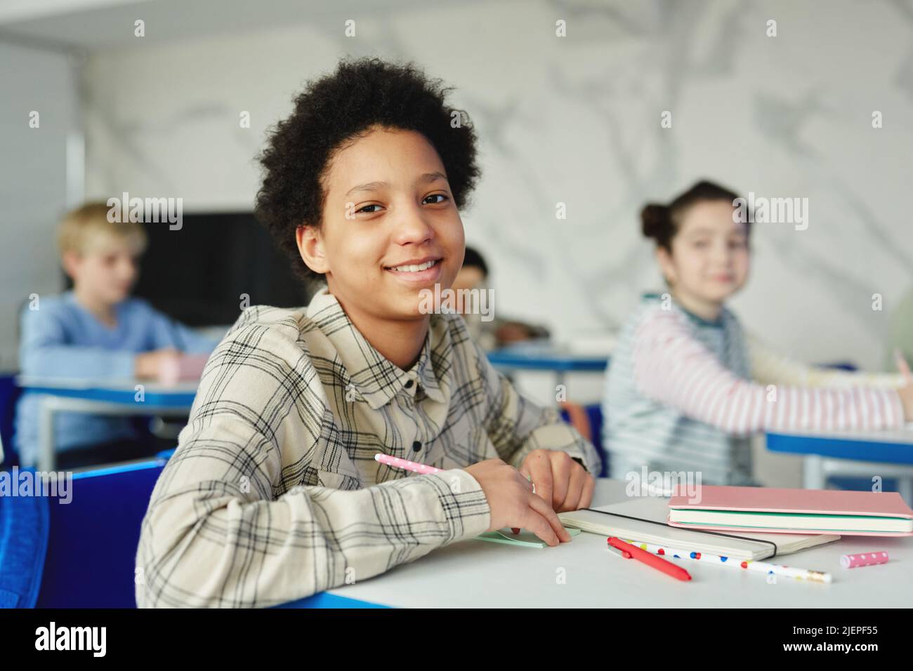Ritratto di sorridente ragazza afroamericana seduta alla scrivania a scuola e guardando la macchina fotografica Foto Stock