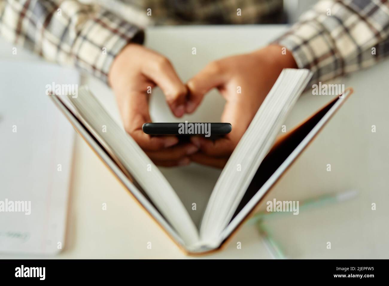 Vista dall'alto primo piano di un telefono nascosto per bambini irriconoscibile a scuola e truffa durante la lezione Foto Stock