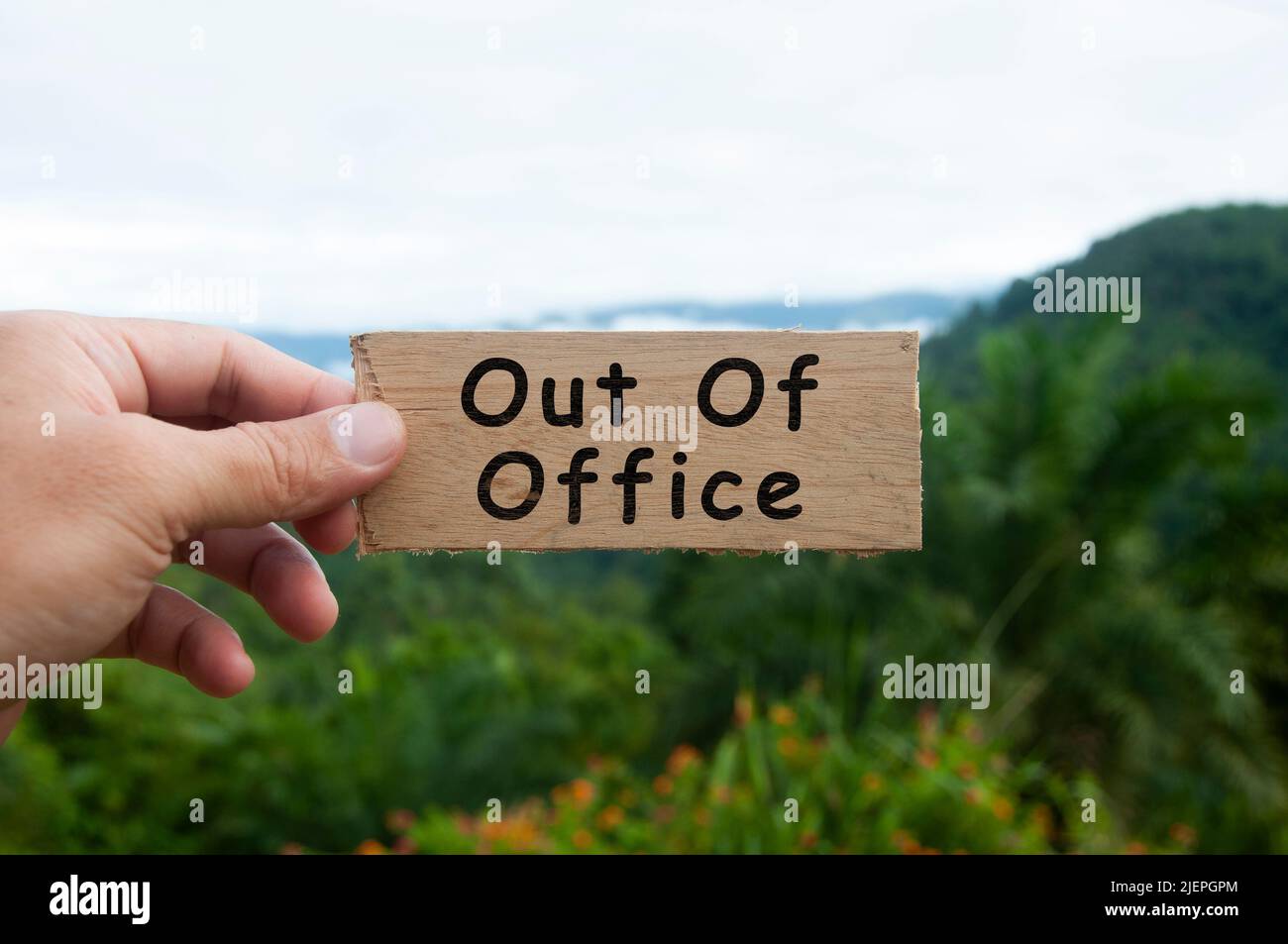 Mano che tiene banner in legno con testo - fuori ufficio. Foto Stock