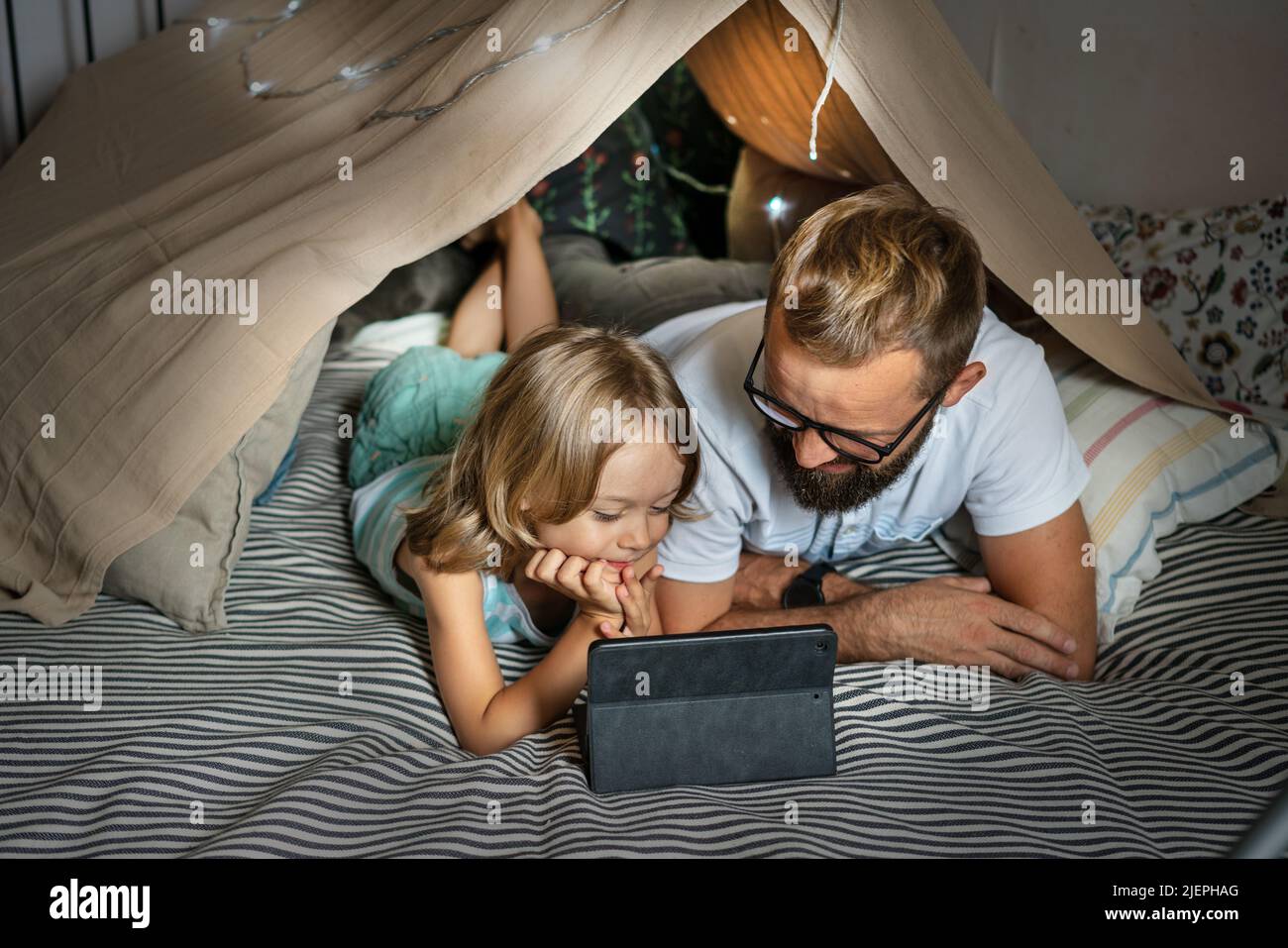 Ritratto di un ragazzo di 6 anni e suo padre che si divertono a giocare in tenda teepee. Padre e figlio usano un tablet digitale per guardare cartoni animati o giocare a giochi per computer che si trovano nella tenda del bambino a casa. Foto Stock
