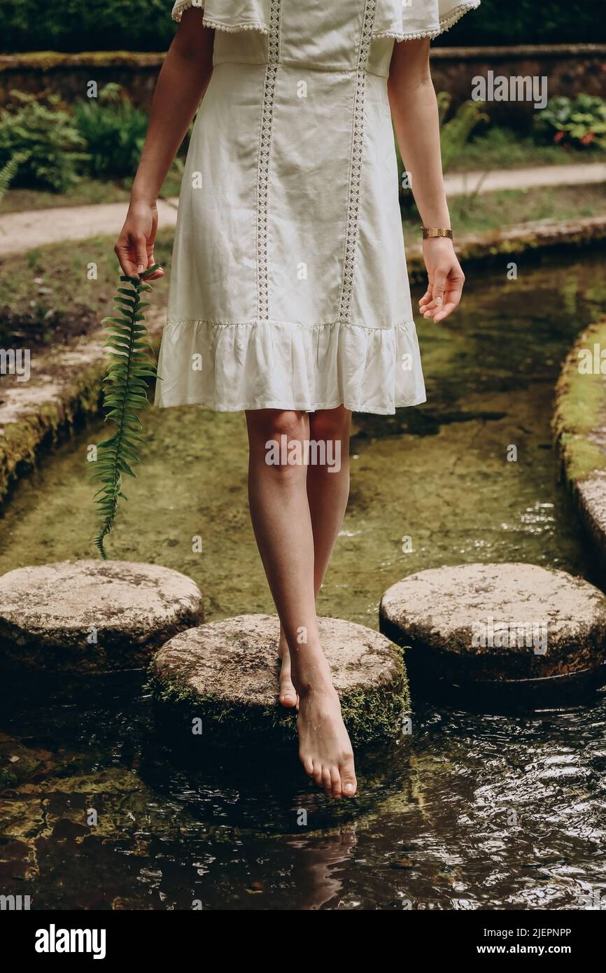 Donna con felce in mano in piedi su pietre e provare l'acqua il giorno d'estate. Concetto di natura estiva Foto Stock