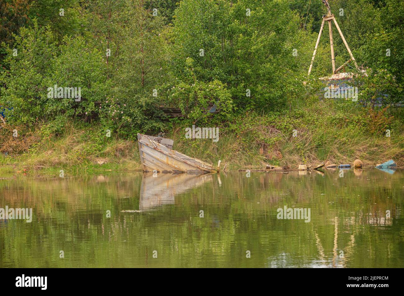 Dalla superficie di un fiume sporge l'arco di una barca dilapidata e abbandonata. Arbusti e alberi sono sullo sfondo. Foto Stock