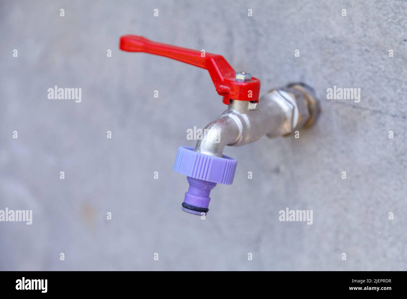 Rubinetto d'acqua in metallo posto sulla strada per l'irrigazione di alberi e fiori sulla casa trama. Foto Stock