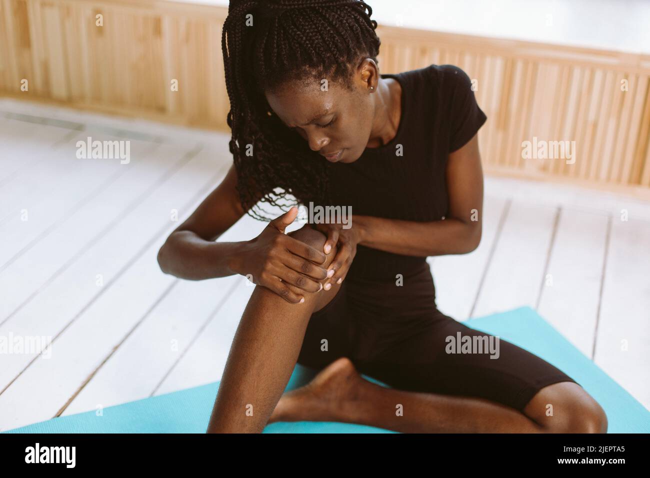 Ritratto di forte pelle scura afroamericana sportiva con dreadlocks stretching, facendo yoga. Dolore al ginocchio, spasmo Foto Stock