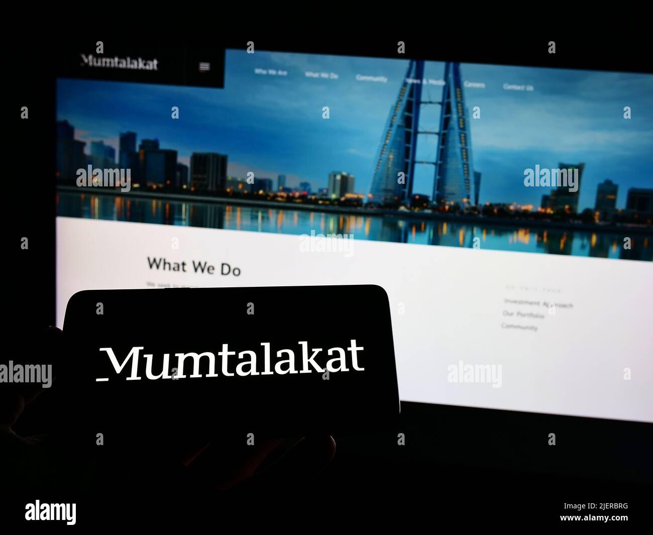 Persona che tiene il cellulare con il logo di Bahrain Mumtalakat Holding Company sullo schermo di fronte al sito web aziendale. Mettere a fuoco sul display del telefono. Foto Stock
