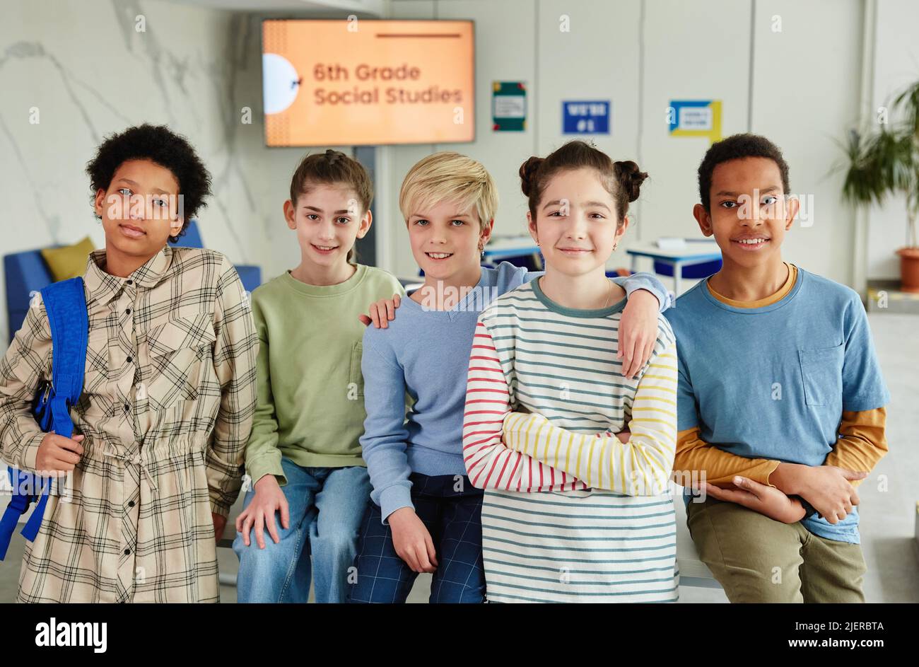 Ritratto di diversi gruppi di bambini che guardano la macchina fotografica e sorridono mentre si levano in piedi insieme in aula scolastica Foto Stock