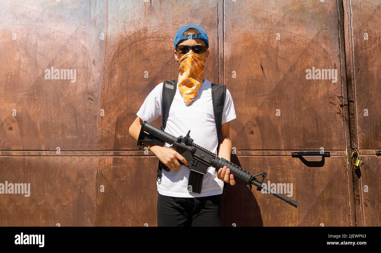 Un bambino che tiene un fucile automatico che indossa una bandana. Concetto di sparatutto per la scuola Foto Stock