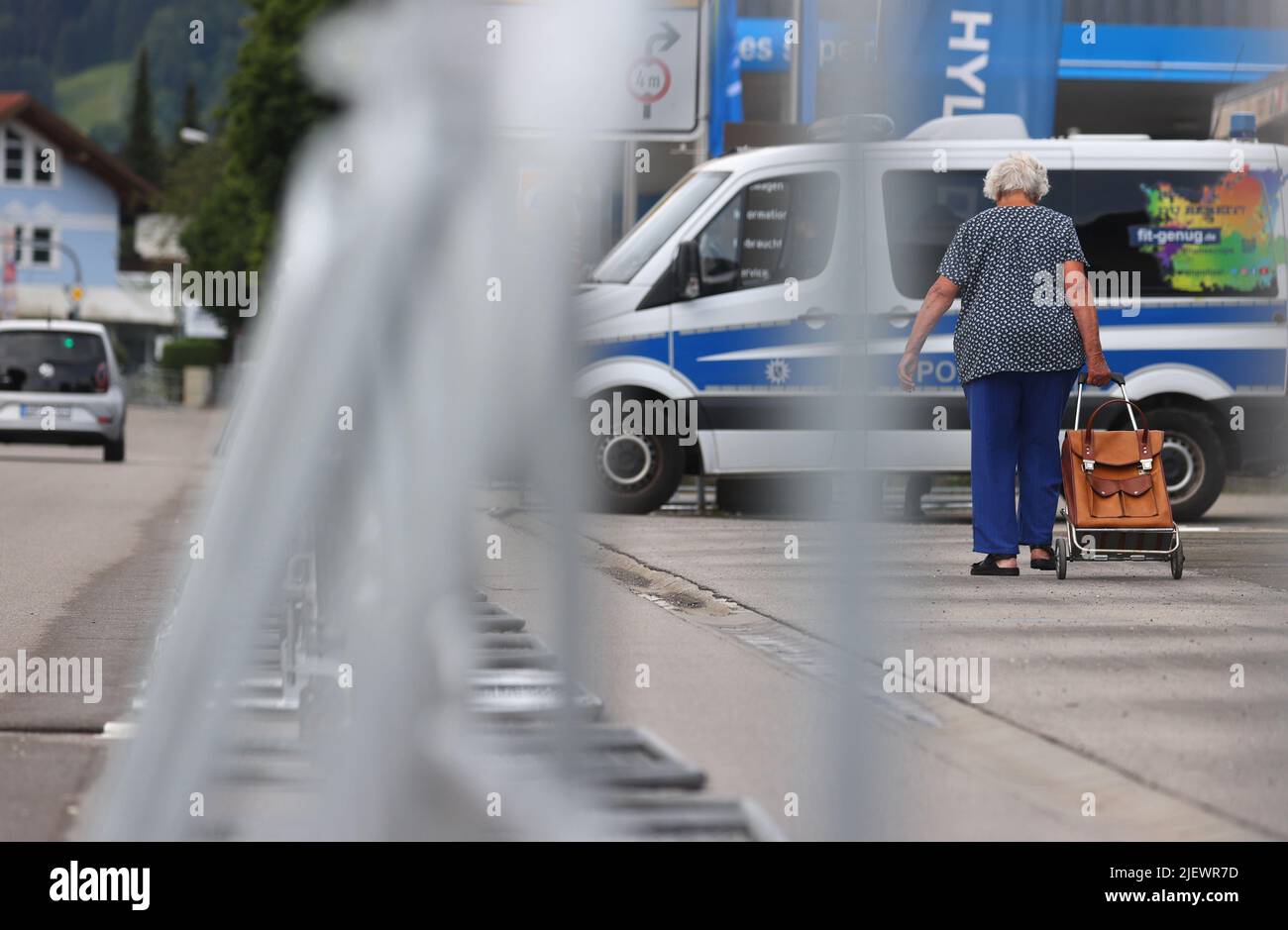 Garmisch Partenkirchen, Germania. 28th giugno 2022. Una donna anziana cammina con una borsa vicino alle barriere e di fronte ad una macchina della polizia. La Germania ha ospitato il vertice del G7 a Schloss Elmau. Credit: Karl-Josef Hildenbrand/dpa/Alamy Live News Foto Stock