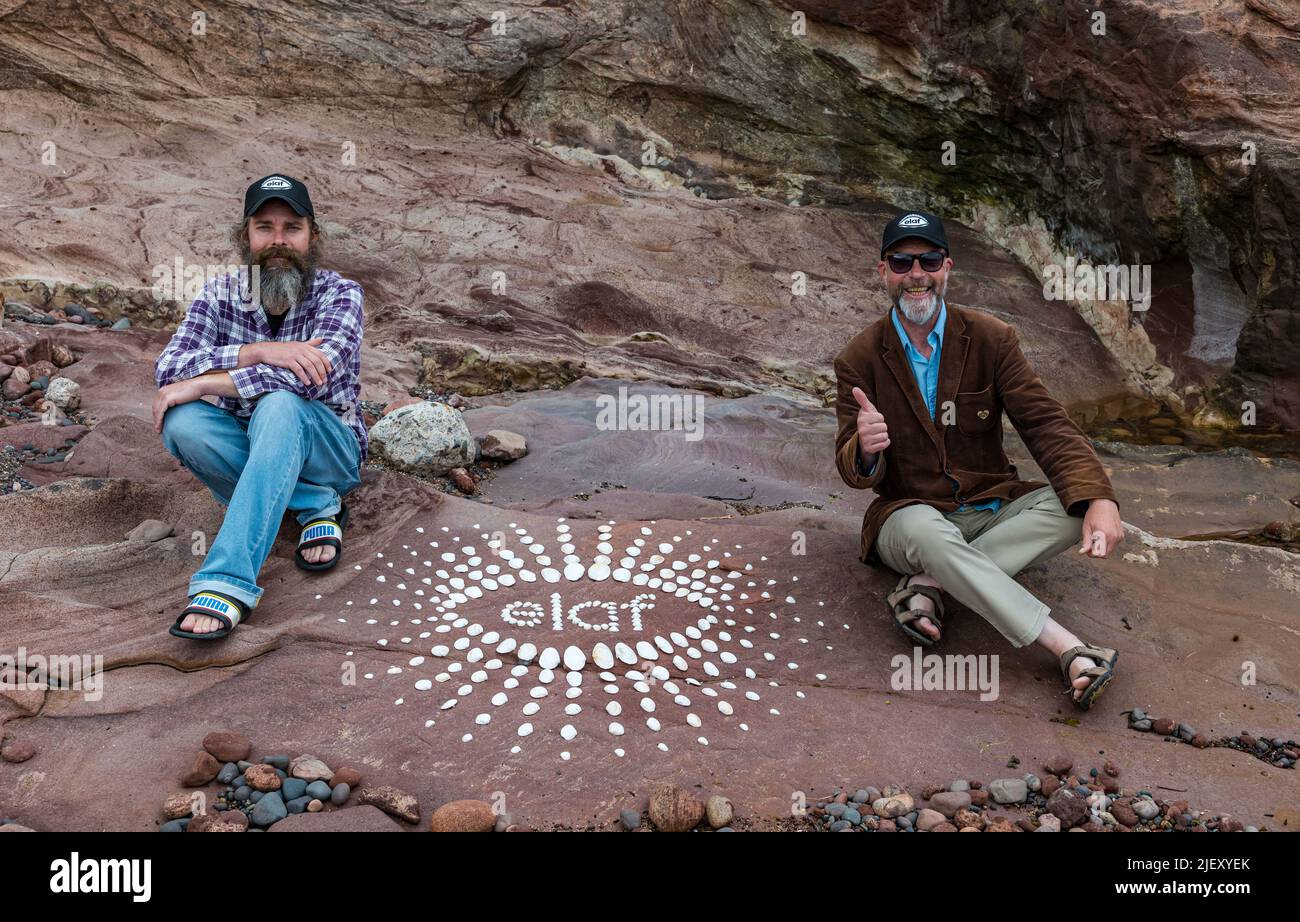 Dunbar, East Lothian, Scozia, Regno Unito, 28th giugno 2022. European Land Art Festival & European Stone Stacking Championships: L'ESSC annuale di quest'anno si è trasformata in un festival di una settimana di arte della terra a partire da lunedì prossimo, che si svolge in luoghi di tutta la città. L'organizzatore James Craig Page e alcune installazioni sulla spiaggia di Eye Cave in preparazione all'evento. Nella foto: Sterling Gregory, uno dei giudici e James Craig Page con un logo artistico realizzato con conchiglie Foto Stock