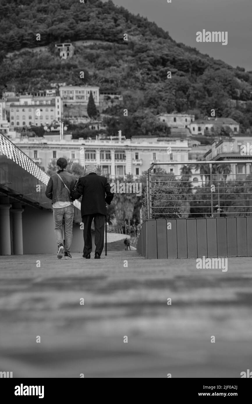 Un'immagine in scala di grigi di un vecchio uomo e di una giovane donna che cammina Foto Stock