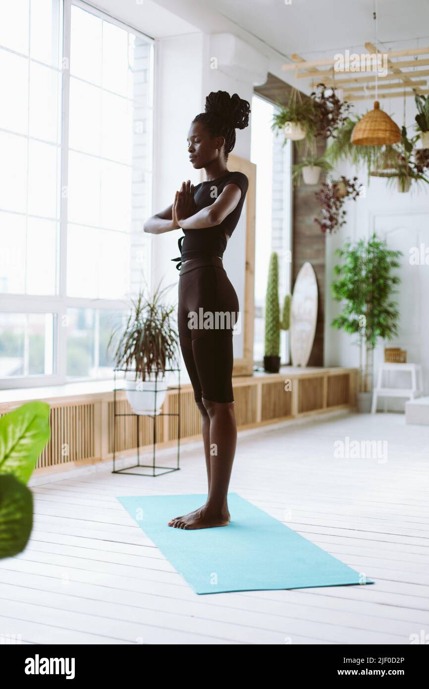 Verticale gioiosa meditante giovane afroamericana in nero sportswear praticare yoga, tenere le mani in namaste mudra Foto Stock