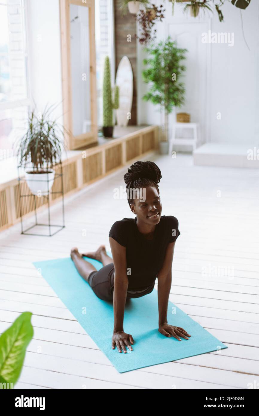 Verticale sorridente pelle scura afroamericana fa esercizi, yoga. Distenditi in posa di cobra asana. Salute e cura del corpo Foto Stock