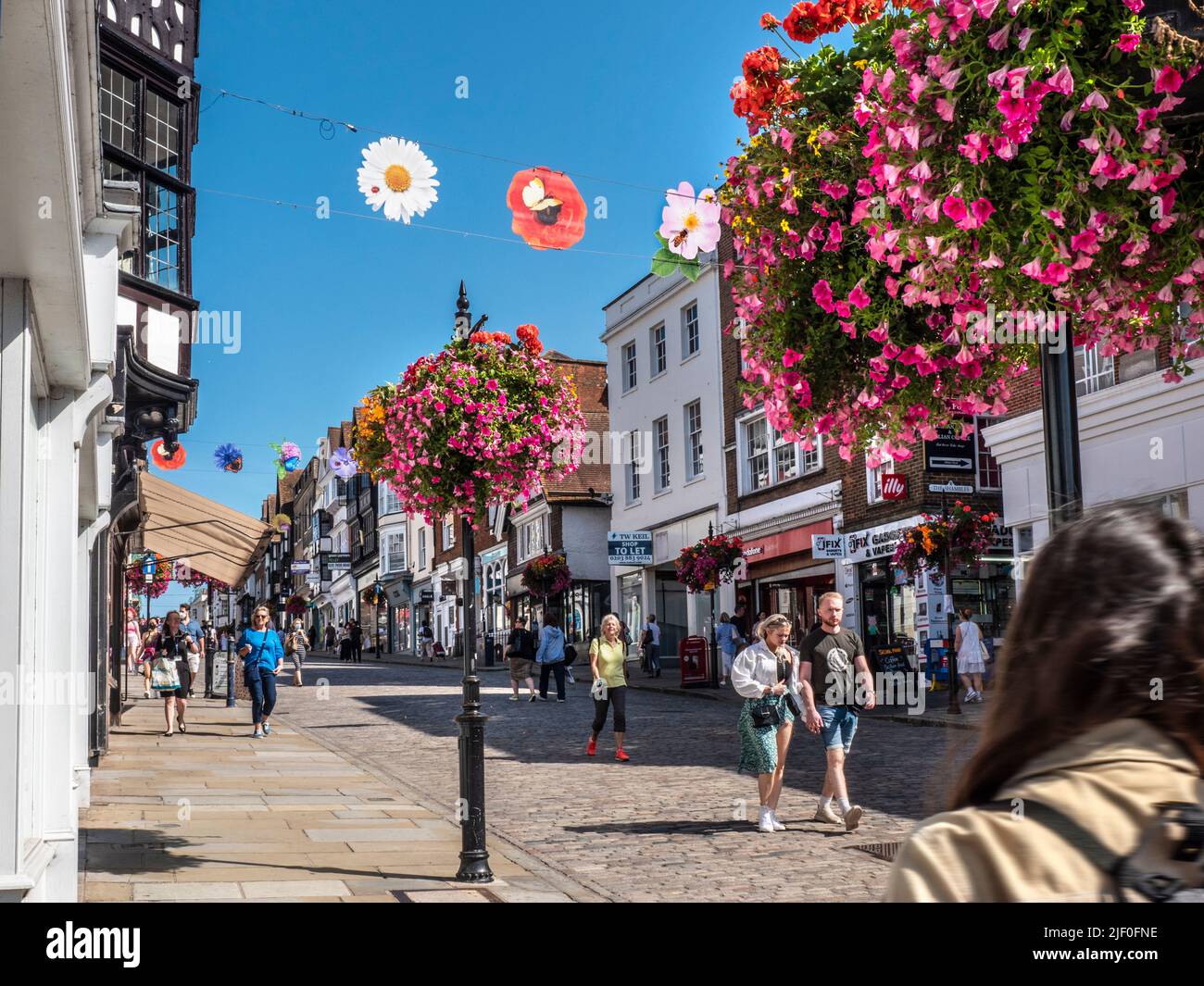 Negozi e negozi di Guildford High Street, cesti di fiori primaverili e colorati striscioni stagionali in blu chiaro caldo sole Guildford Surrey UK Foto Stock