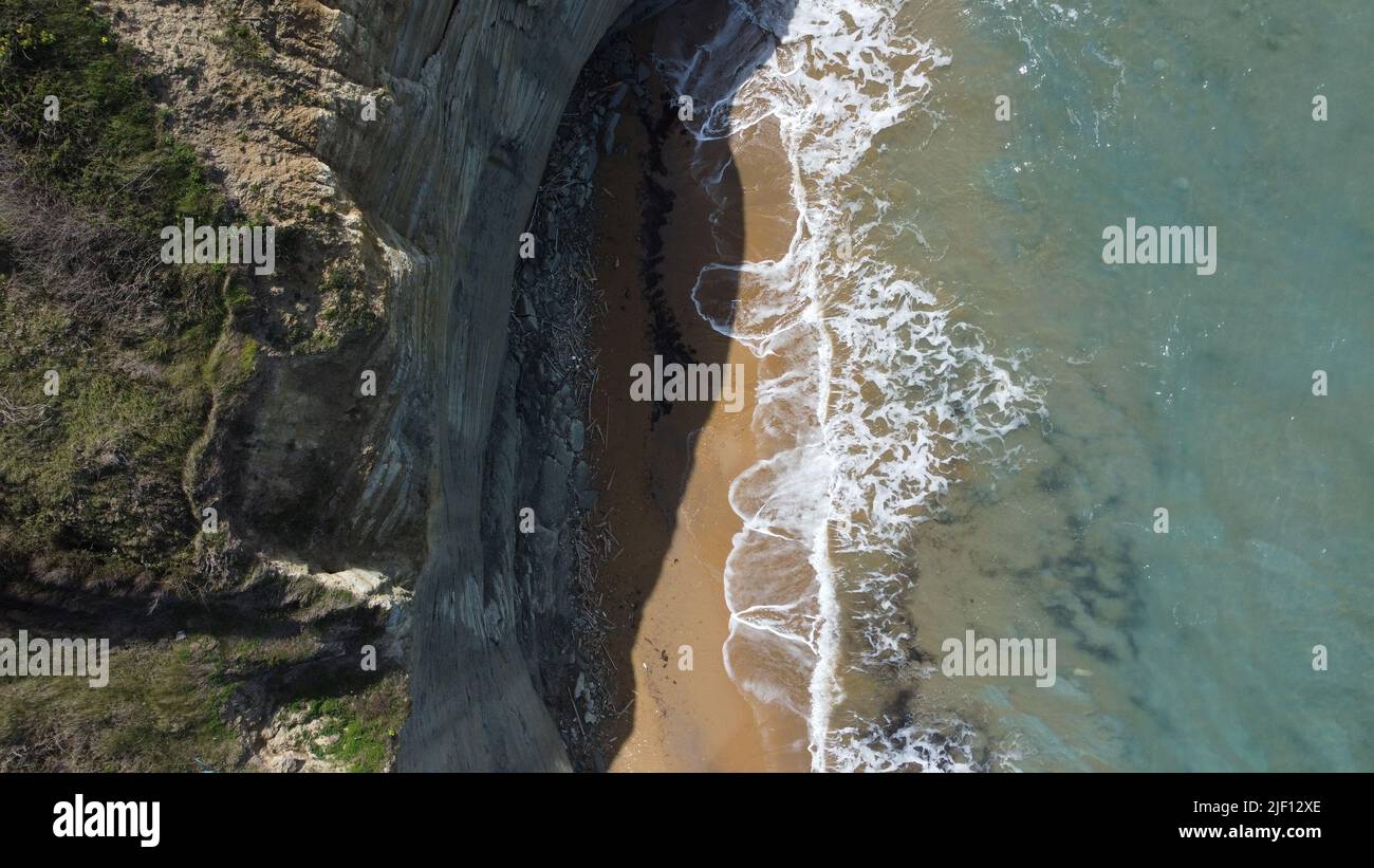 Una vista aerea dall'alto di una spiaggia sabbiosa sotto scogliere boscose bagnate da onde di mare turchesi Foto Stock