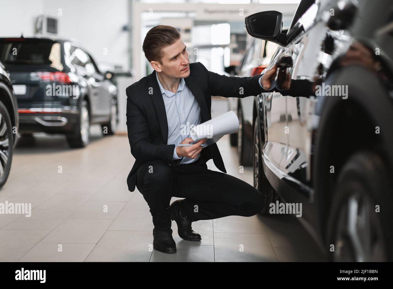 Bel direttore di vendita giovane facendo nuovo check up auto al salone di lusso auto, a tutta lunghezza Foto Stock