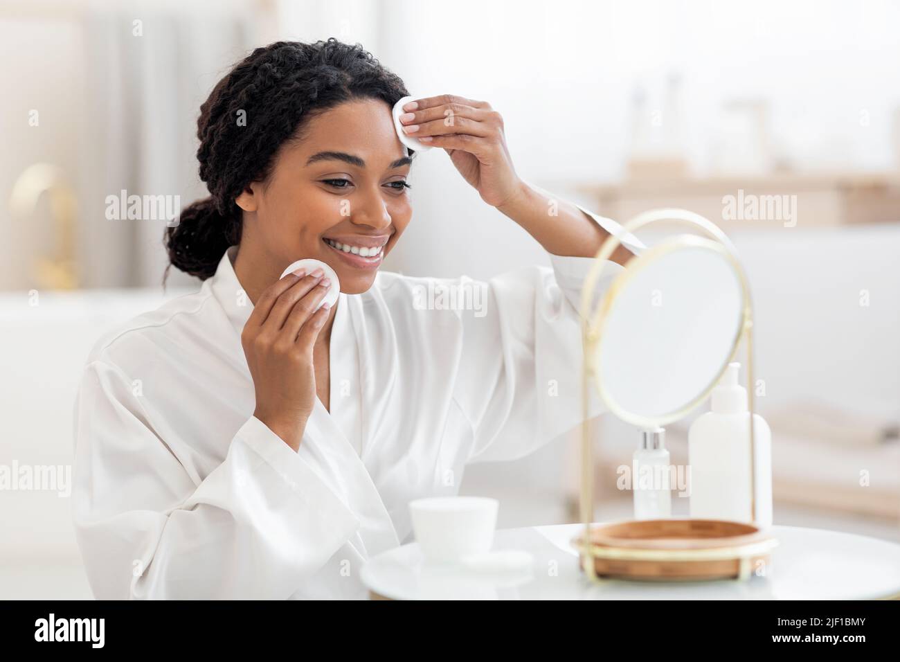 Routine di bellezza. Smiling Black Female Looking in Specchio e pulizia della pelle Foto Stock