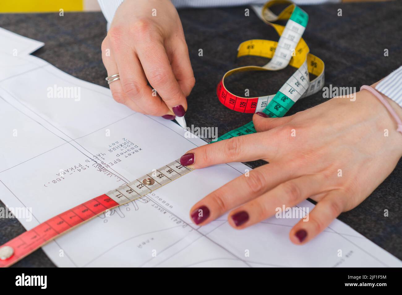 Il dressmaker contrassegna un pezzo di tessuto con gesso in base al modello di carta. Lavoro di sarto, utensili per cucire Foto Stock